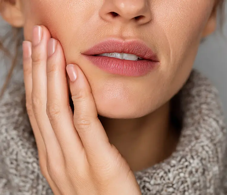 &bdquo;Nahaufnahme des unteren Gesichts einer Frau. Sie legt ihre Hand an die Wange, die Lippen sind leicht ge&ouml;ffnet und die Z&auml;hne sichtbar.