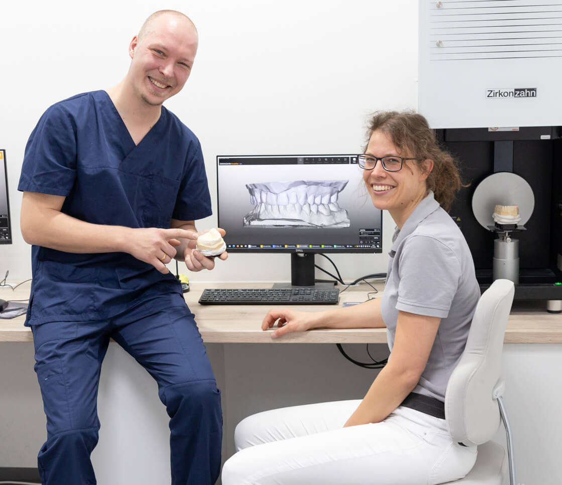 Chirurg und Zahntechniker besprechen gemeinsam einen Fall anhand eines 3D-Modells und l&auml;cheln in die Kamera